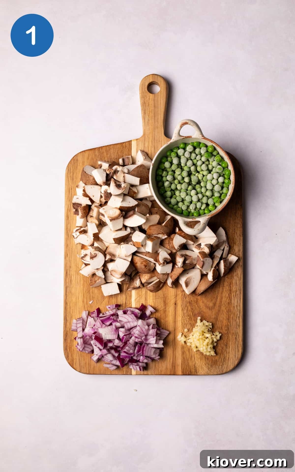 Freshly chopped red onion, crushed garlic, and sliced chestnut mushrooms on a wooden cutting board.
