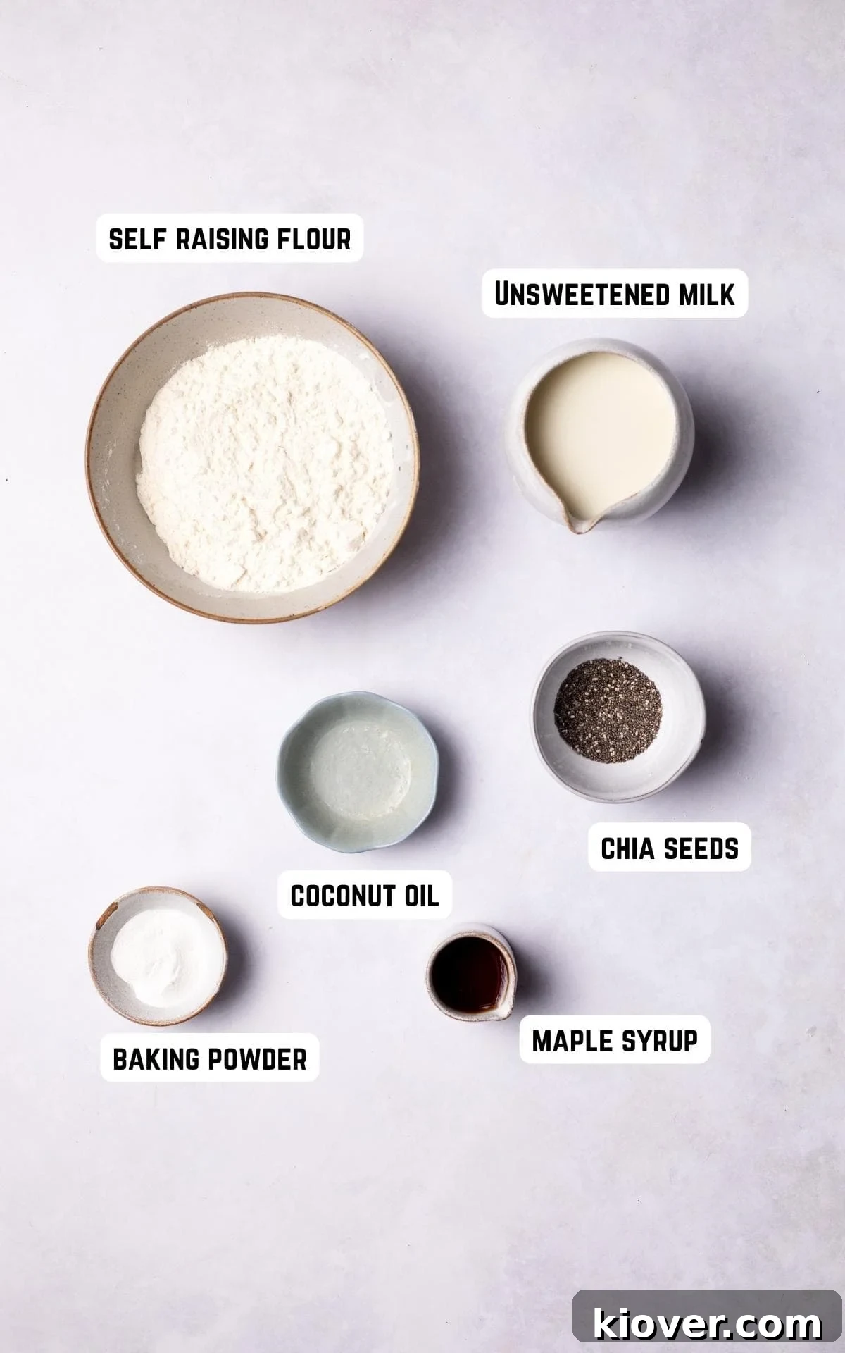 Key ingredients for making gluten-free pancakes, including flour, baking powder, chia seeds, coconut oil, maple syrup, and plant-based milk, arranged on a white marble background.