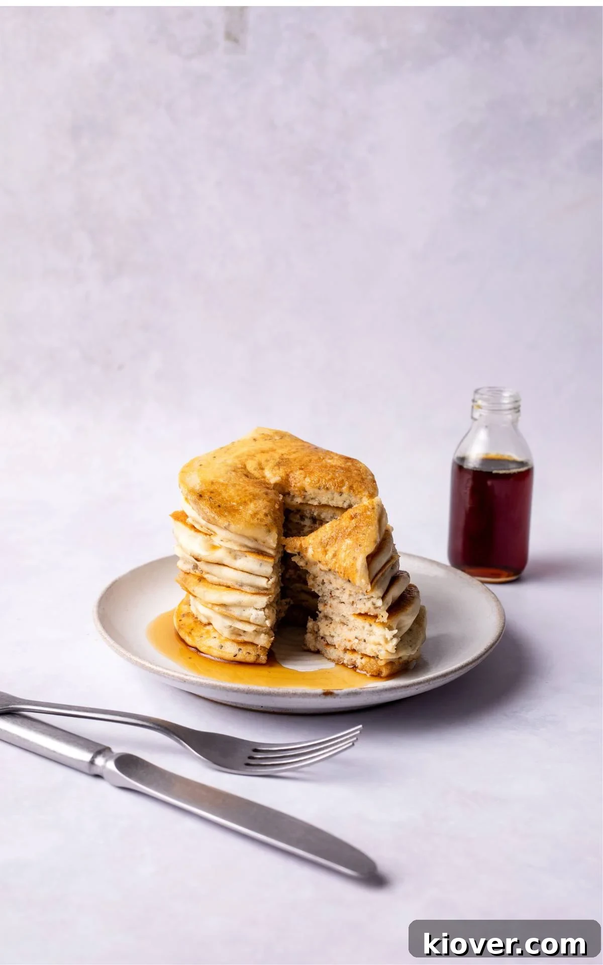 A stack of perfectly golden gluten-free pancakes on a white plate, garnished with fresh berries and a generous pour of maple syrup, inviting you to enjoy a delicious breakfast.