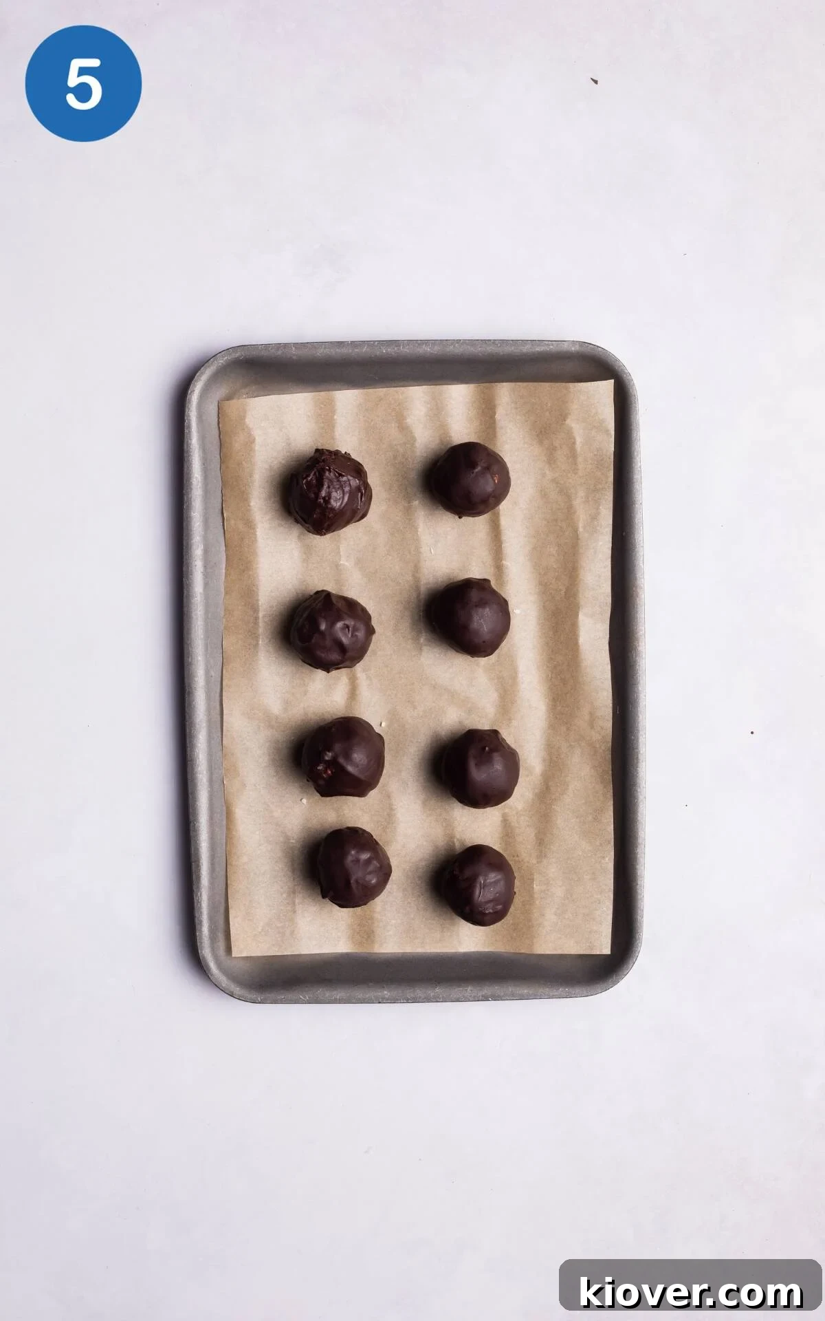 Chilled coconut balls being coated in smooth chocolate sauce, ready for final freezing.