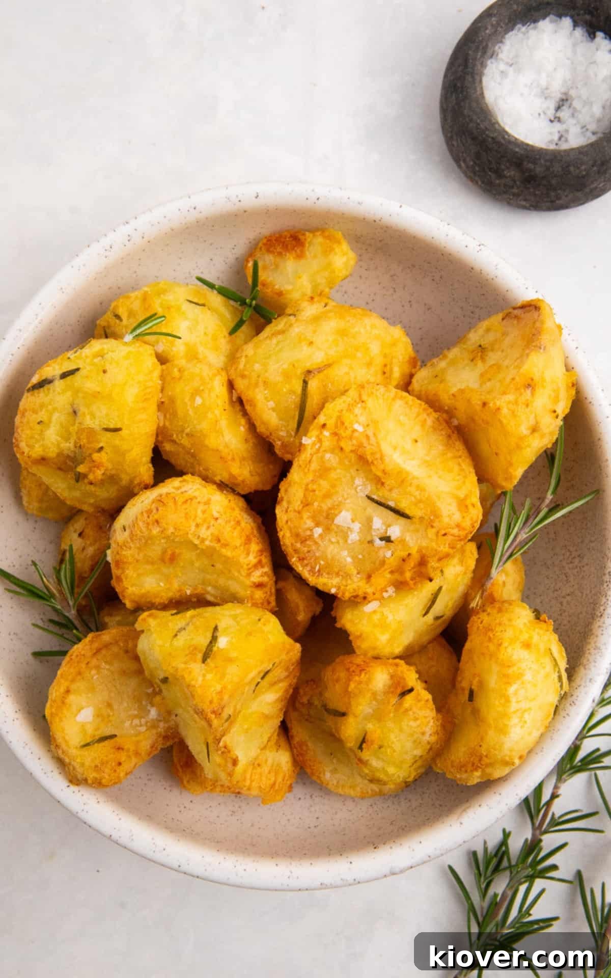 air fryer roast potatoes in a white bowl served with fresh rosemary and flaked sea salt.