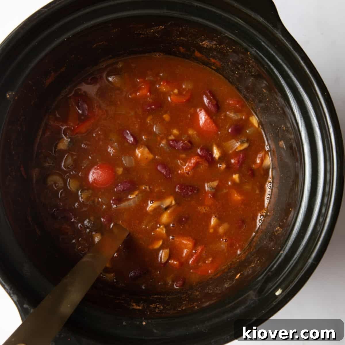 Overhead shot of rich, slow-cooked vegan chilli in a ceramic slow cooker with a ladle, ready to be served.
