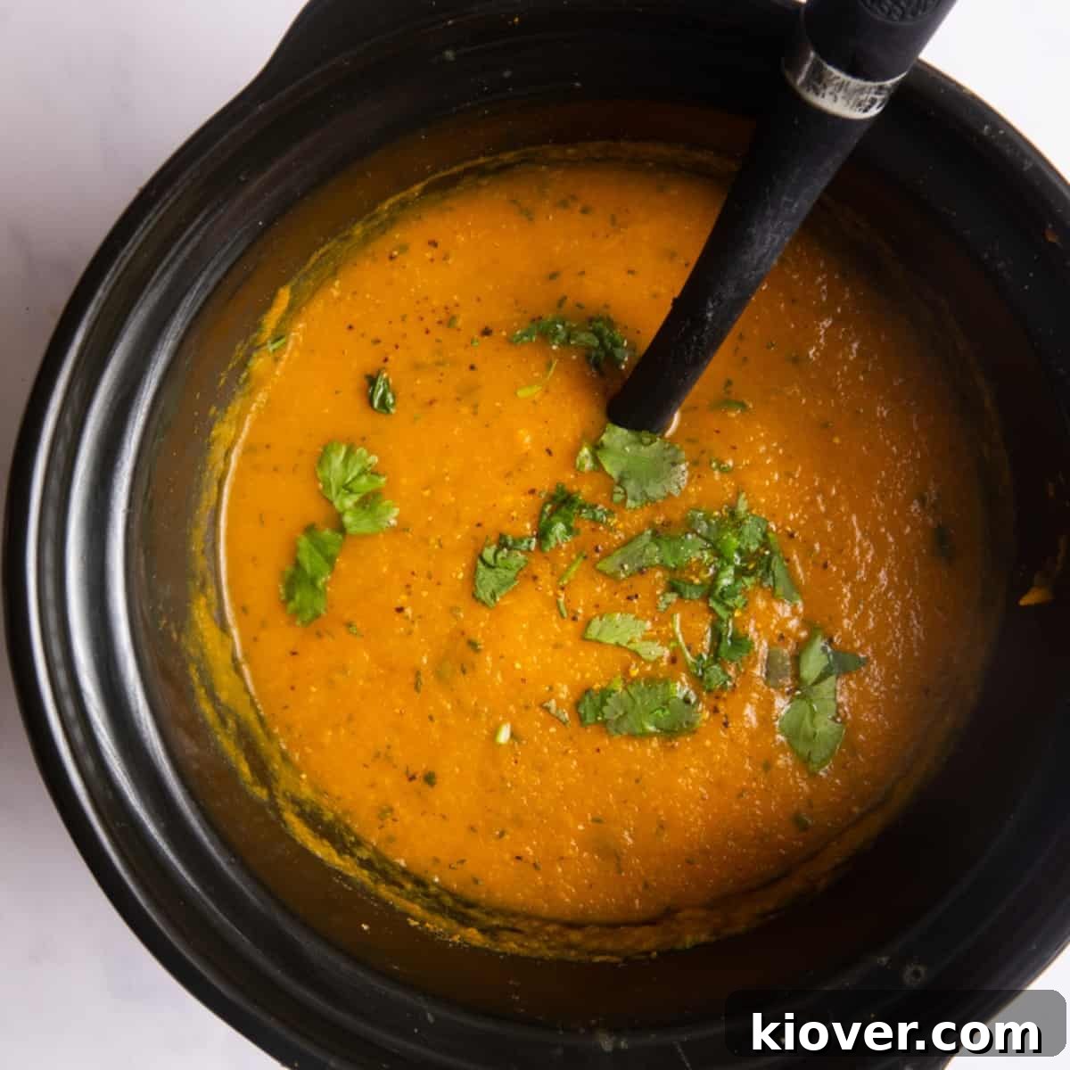 Overhead shot of creamy Slow Cooker Carrot and Coriander Soup, garnished with fresh coriander, served directly from the slow cooker with a ladle.