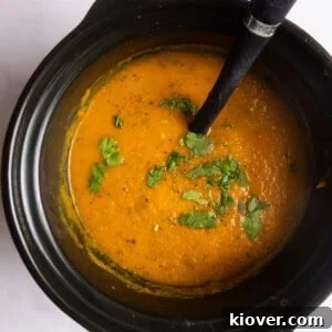 Overhead shot of blended carrot and coriander soup in slow cooker topped with fresh coriander and ladle.