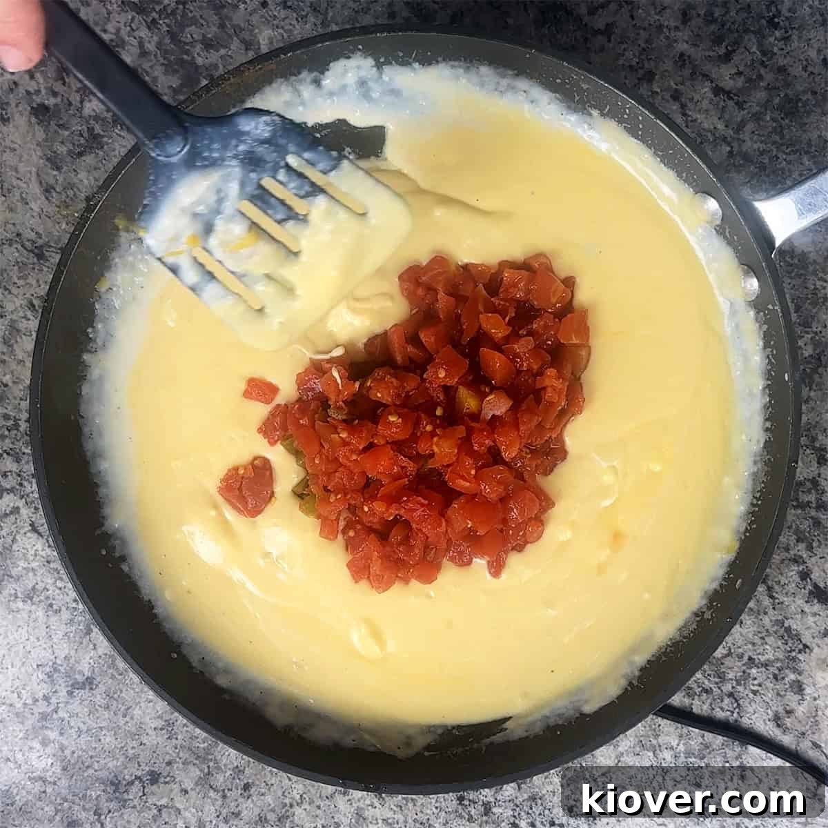A person stirring a pan with cheese and tomatoes.