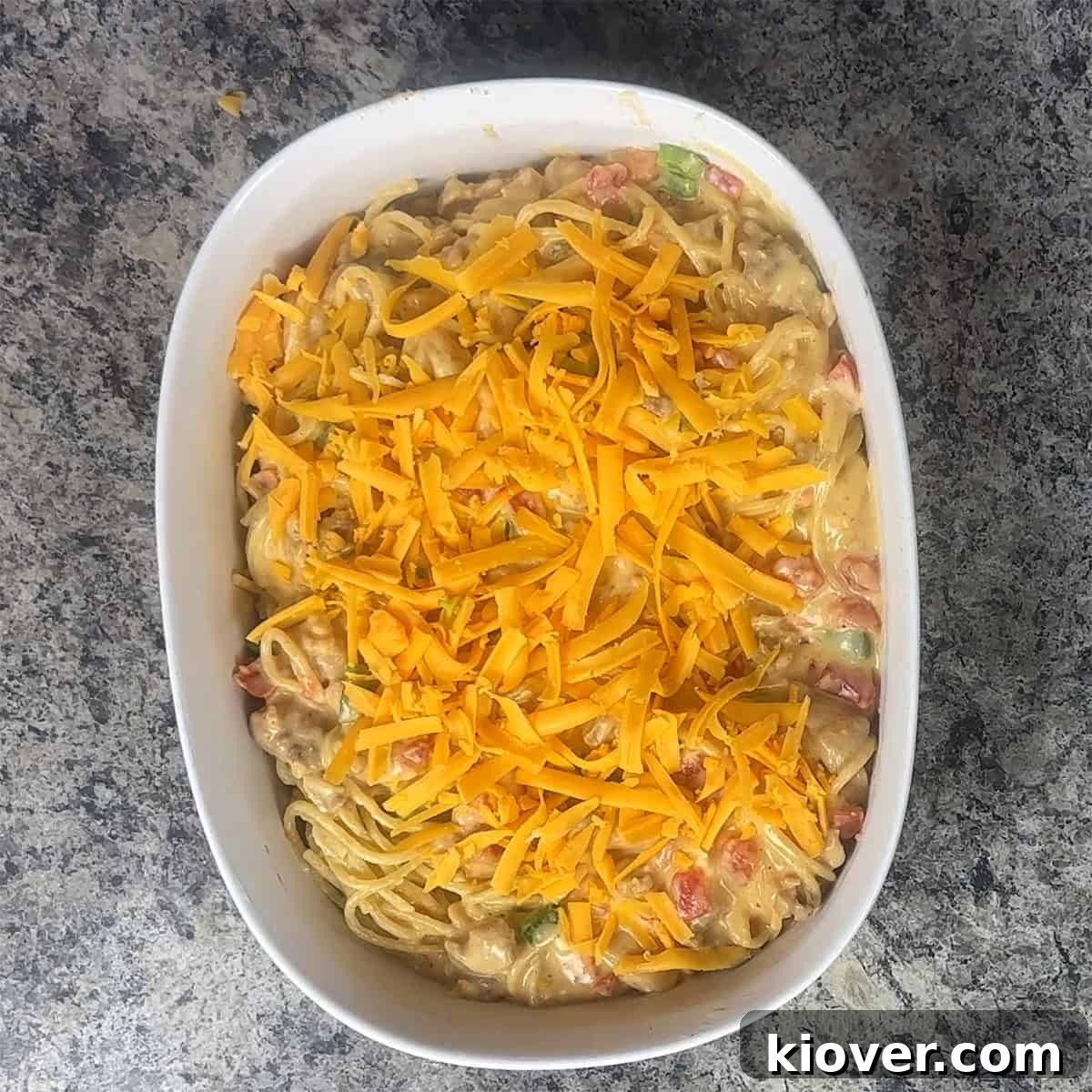 Chicken spaghetti in a casserole dish with unmelted cheese on top.