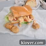 A Po' Boy sandwich on a sandwich paper with french roll in the background