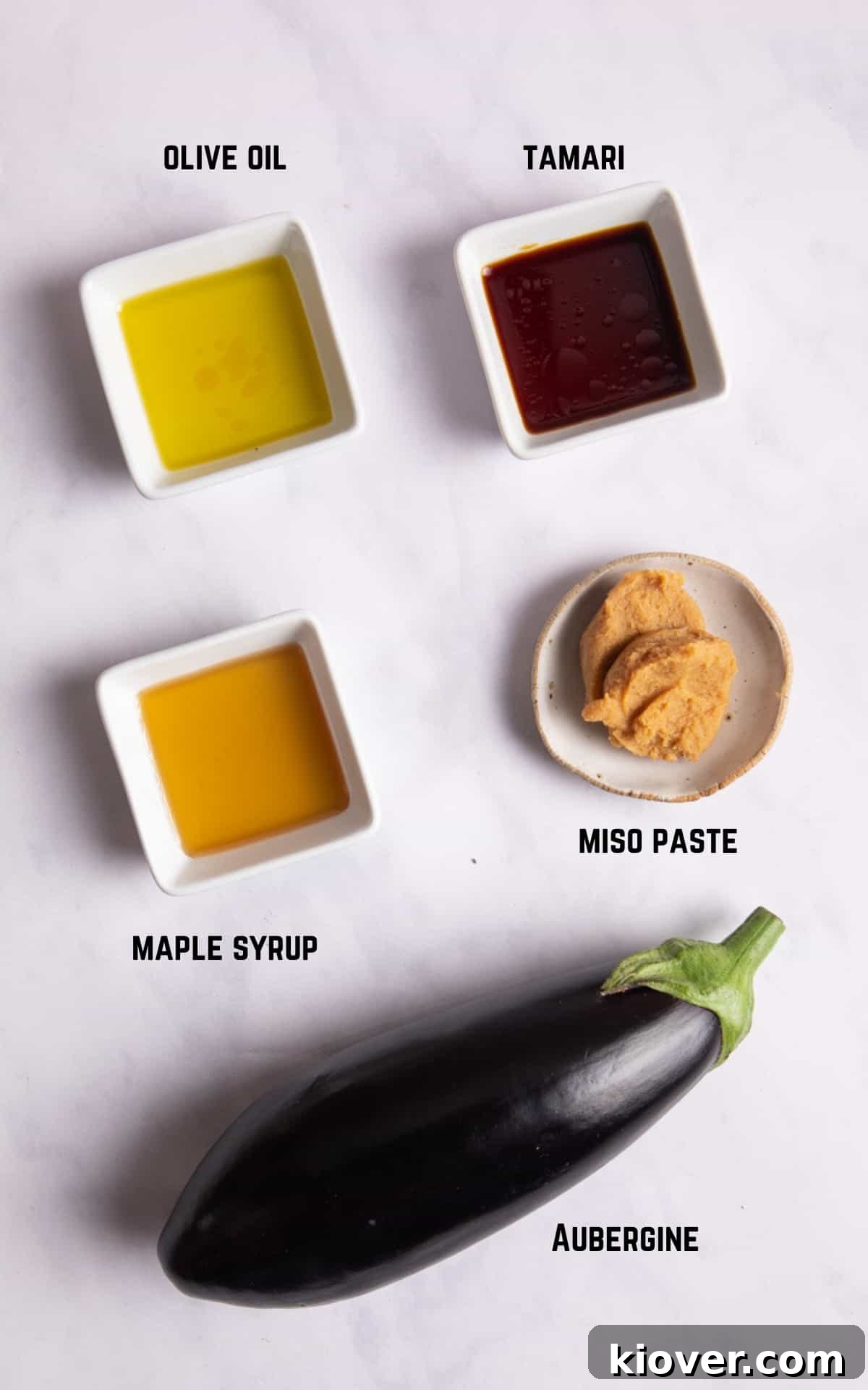 Perfectly Sweet and Savory Miso Glazed Aubergine Nasu Dengaku 3 A collection of the five key ingredients for miso aubergine, neatly arranged on a white surface: two fresh aubergines, a container of white miso paste, a bottle of tamari, a bottle of maple syrup, and a bottle of olive oil.