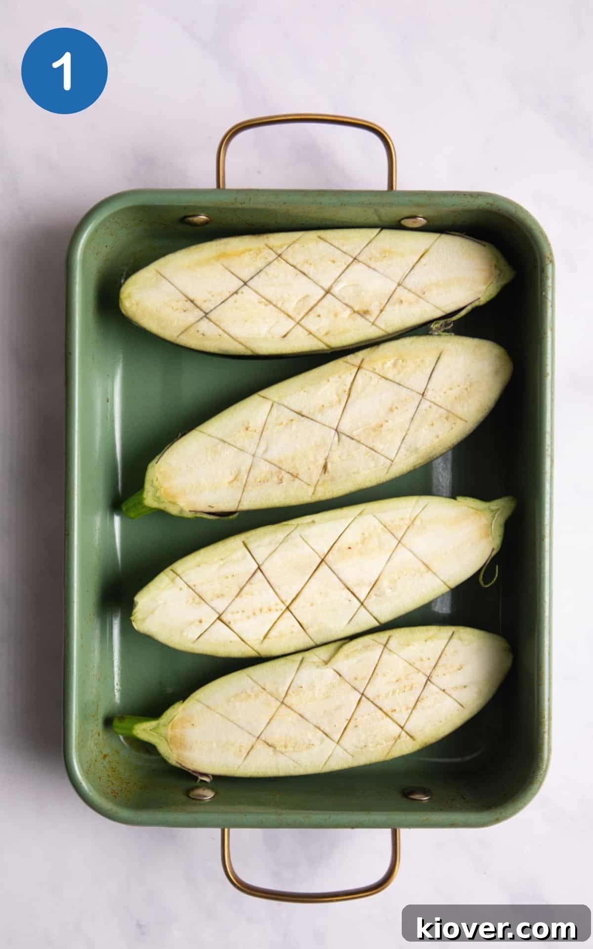 Perfectly Sweet and Savory Miso Glazed Aubergine Nasu Dengaku 4 Two raw aubergines cut in half lengthwise, with deep criss-cross slits scored into their flesh, resting inside a green baking tray, ready for the oven.