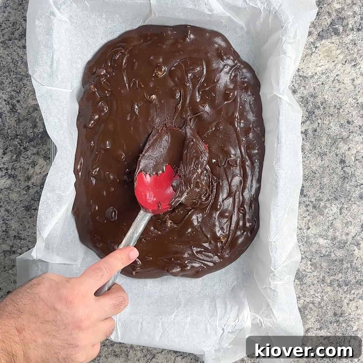 Spreading the warm Velveeta fudge evenly into a parchment-lined dish.