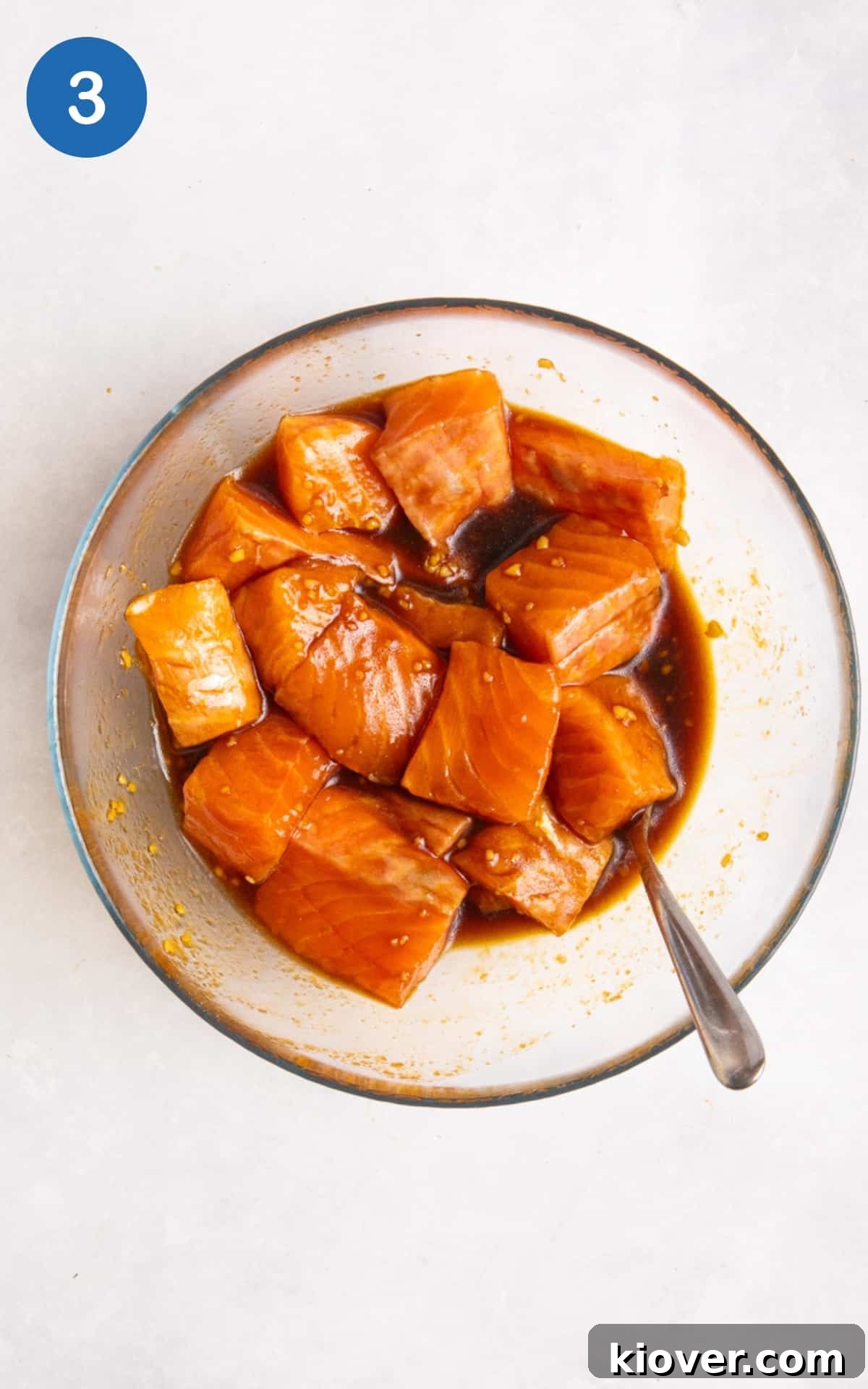 Cubed salmon immersed in a rich, savory marinade in a glass bowl, ready for chilling.