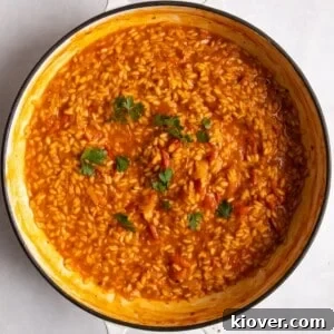 Overhead shot of vibrant tomato risotto in a large, shallow frying pan on a white surface.
