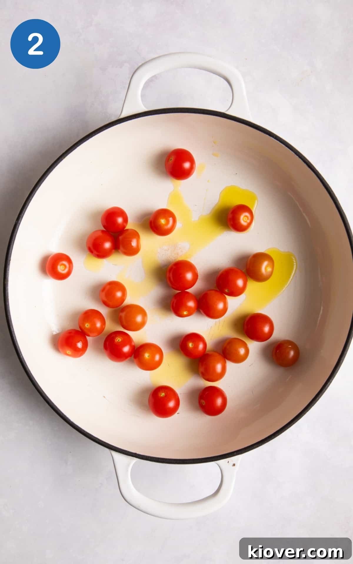 Whole cherry tomatoes glistening with oil in a large non-stick frying pan, beginning to soften.