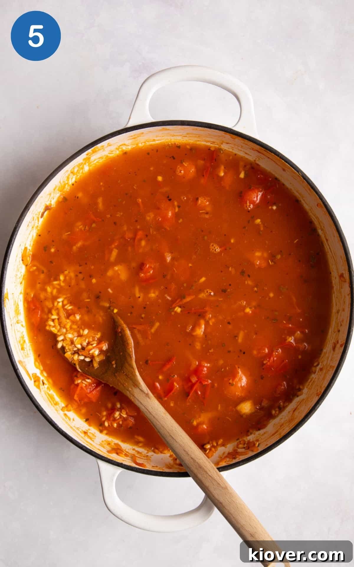 Creamy tomato risotto simmering gently in a large non-stick white frying pan, stirred with a wooden spoon.