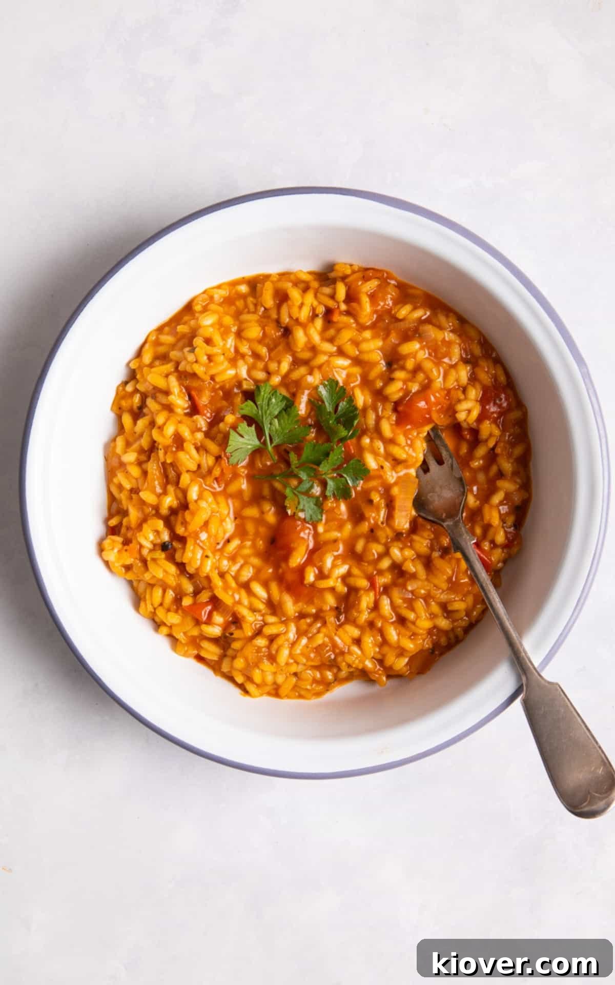 Close-up of a serving of creamy tomato risotto in a white bowl, garnished with a sprig of fresh basil.