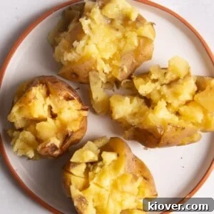 Four jacket potatoes cut open on a plate with melted butter on top.
