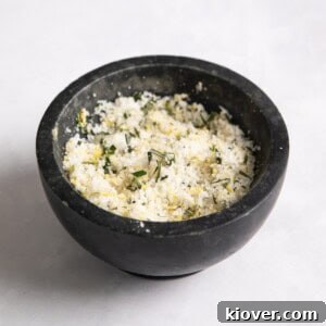A striking close-up of homemade rosemary salt, beautifully presented in a small black pot on a pristine white surface, ready to enhance any dish.