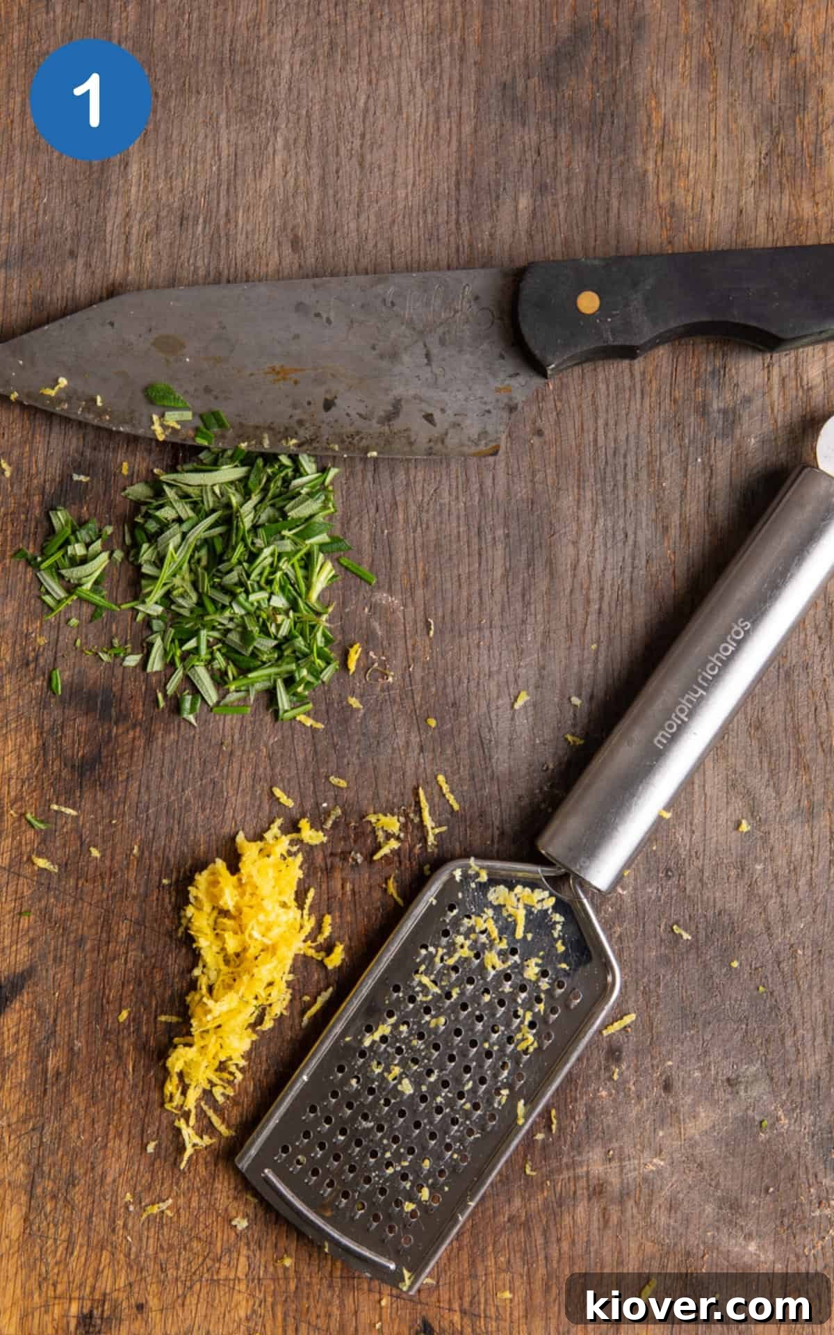 Freshly chopped rosemary and bright lemon zest arranged on a dark wooden chopping board next to a sharp knife, ready for blending into salt.