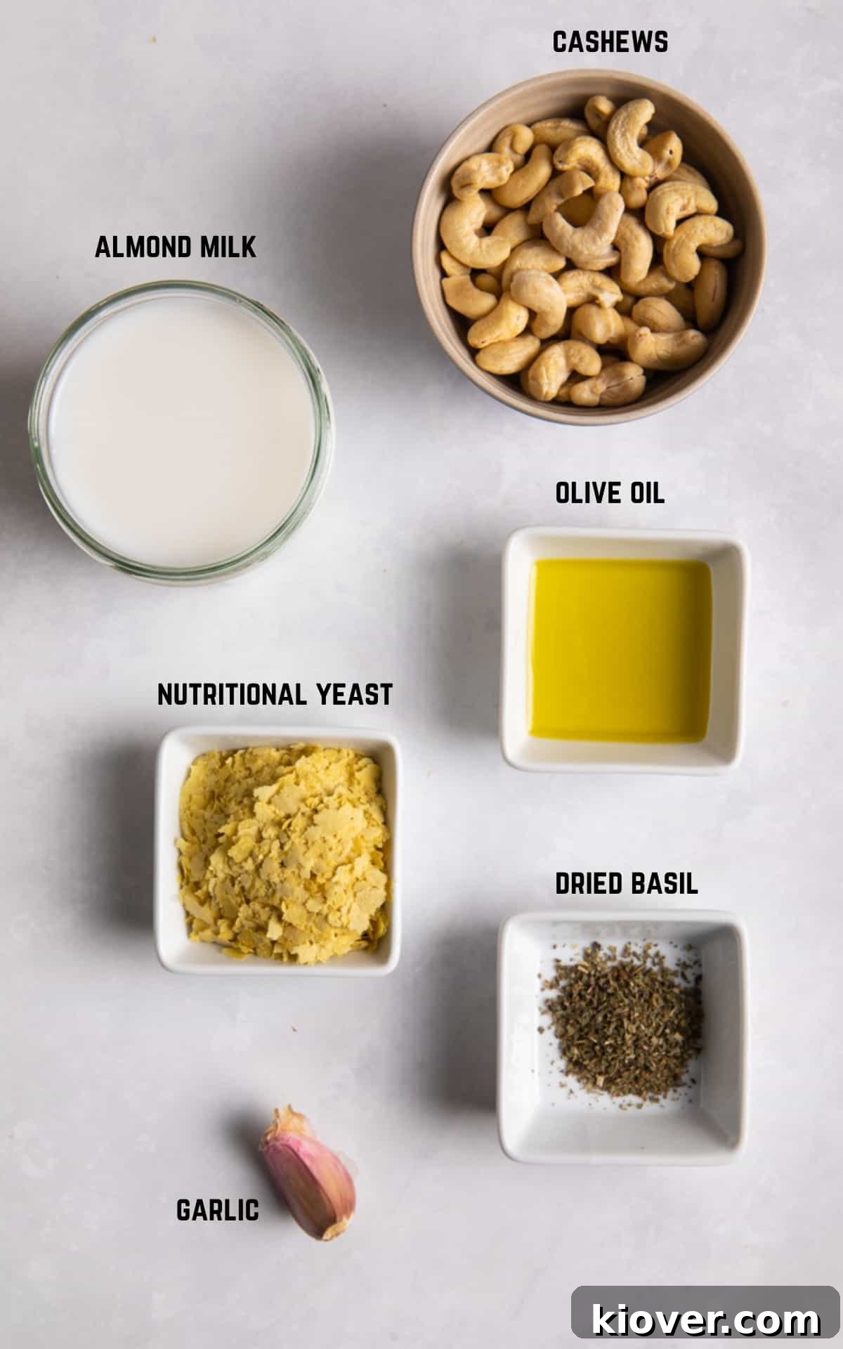 Fresh ingredients for making vegan white sauce, including cashews, nutritional yeast, garlic, and almond milk, neatly arranged on a white surface.