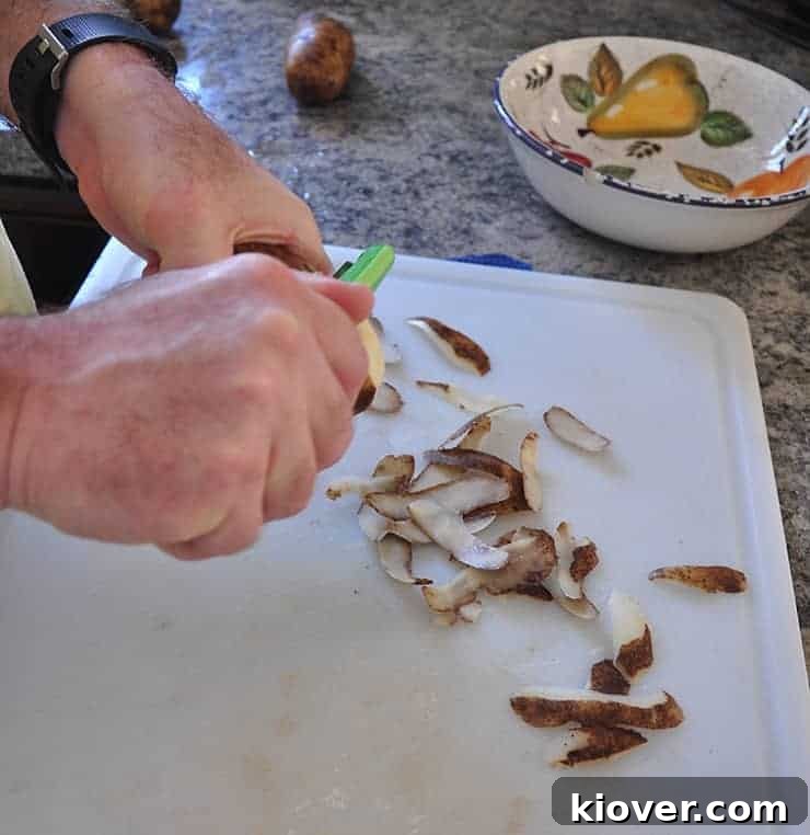 Hands peeling russet potatoes on a wooden cutting board, preparing them for shredding.