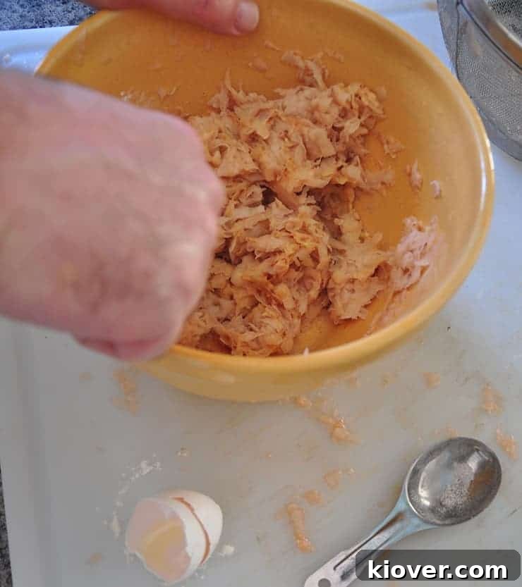 A mixing bowl filled with shredded potatoes, egg, and flour, being combined to form tater tot mixture.