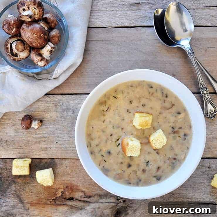Overhead shot of cream of mushroom soup with croutons on top and fresh mushrooms on the side, presented on aged wood.