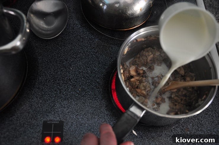 Pouring fresh cream into a simmering mushroom roux, creating a rich and smooth base.