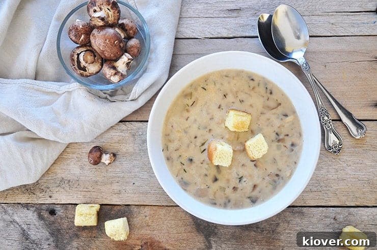 Completed homemade cream of mushroom soup garnished with fresh herbs and croutons, served on an rustic wooden background alongside fresh mushrooms.
