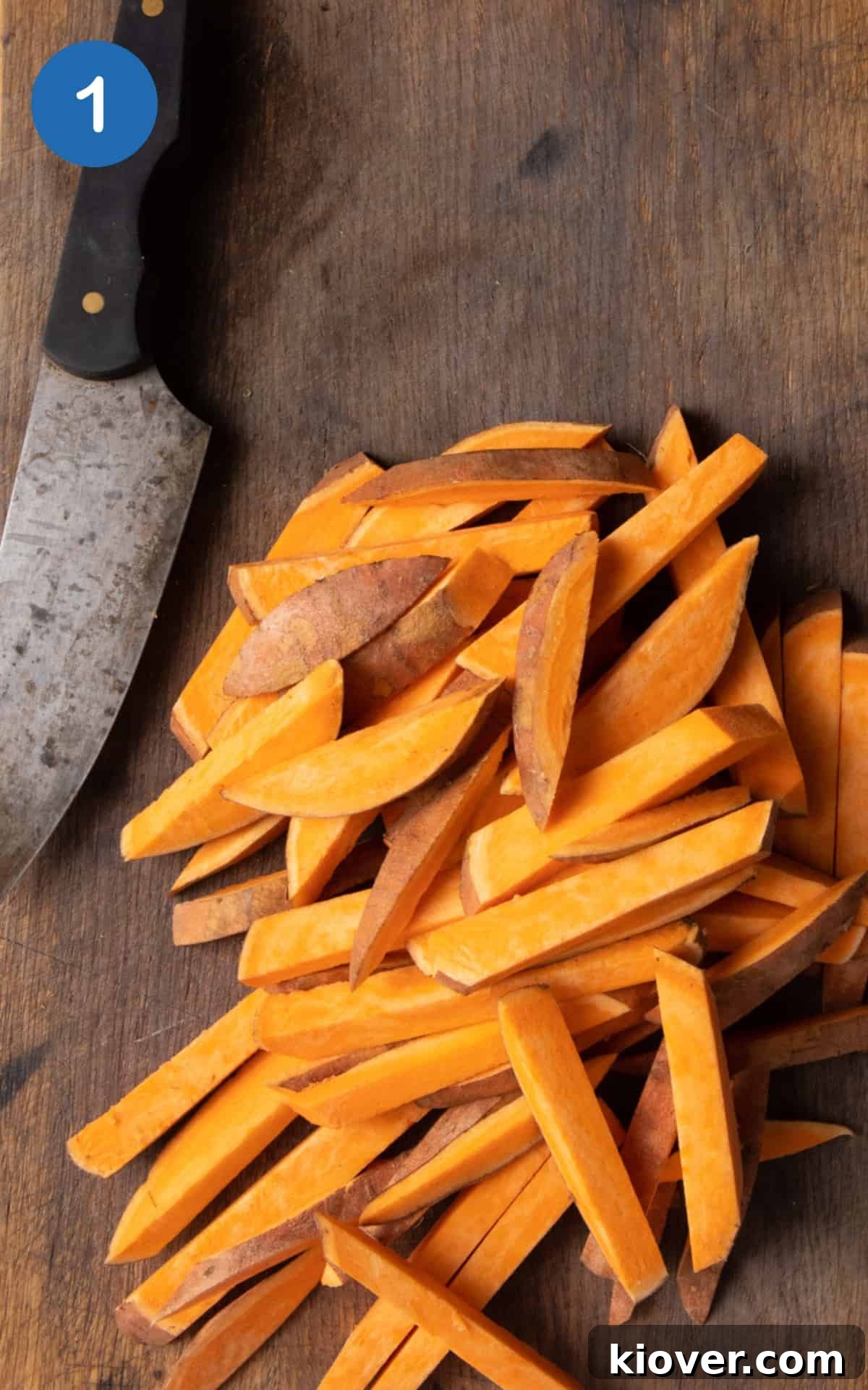 Sweet potatoes cut into chip shapes on dark wooden chopping board.