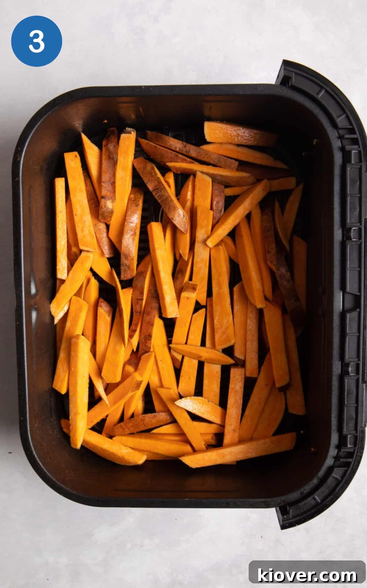 Uncooked Sweet Potato Fries in air fryer on white surface.