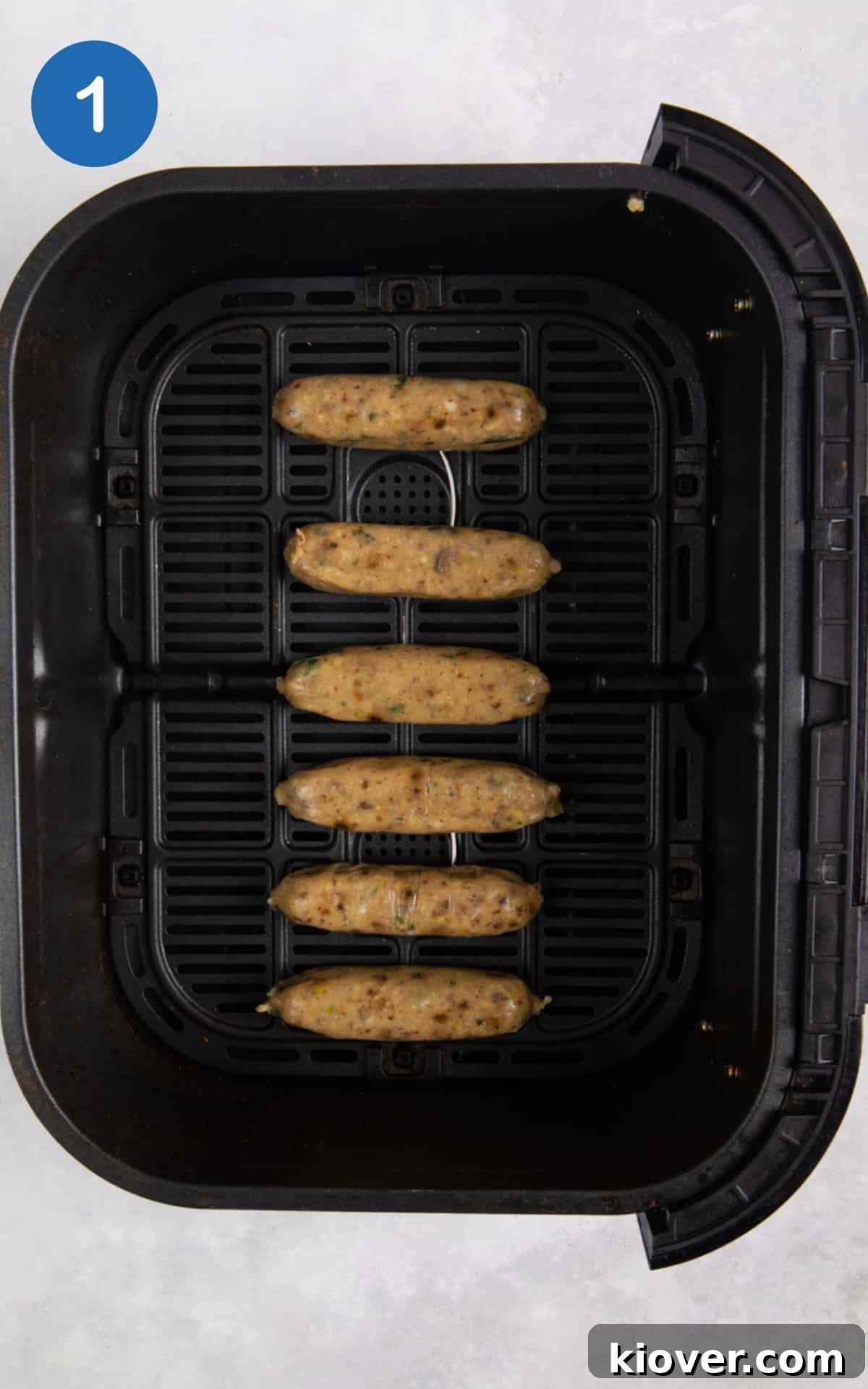 Raw sausages neatly arranged in a single layer inside a black air fryer basket, ready for cooking.
