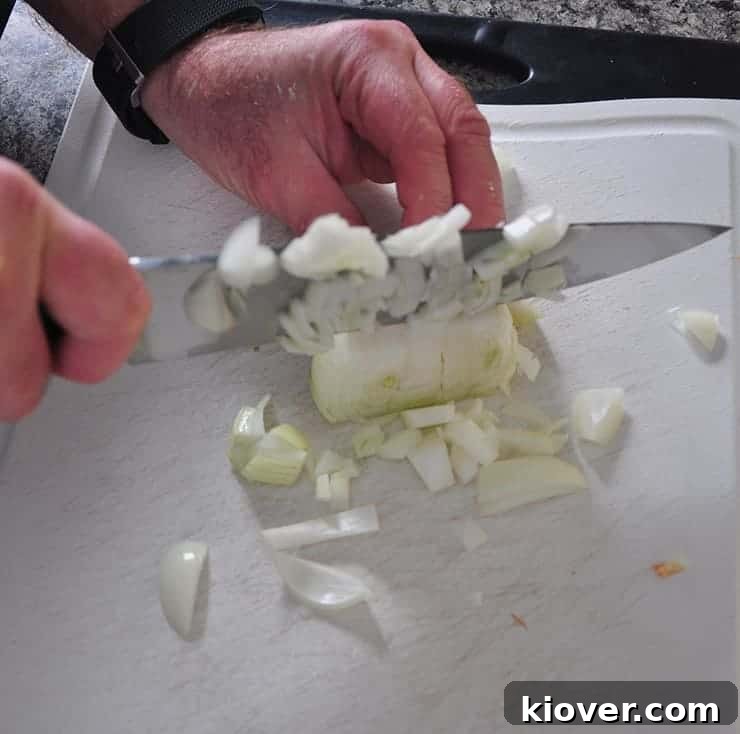 Chopping Onion A chef meticulously chopping a large onion with a high-quality Wustoff knife, in preparation for cooking the hot dish recipe, showcasing the initial steps of the meal preparation.