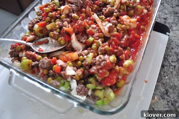 Mixing Hotdish Ingredients A mixed hotdish, not yet baked, settled in a 9 by 13 inch baking dish on a cutting board, with a spoon stirring the ingredients, showcasing the preparation process.