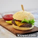 Food processor ground patty burgers on a wood plank with a pickle and ketchup in the background.