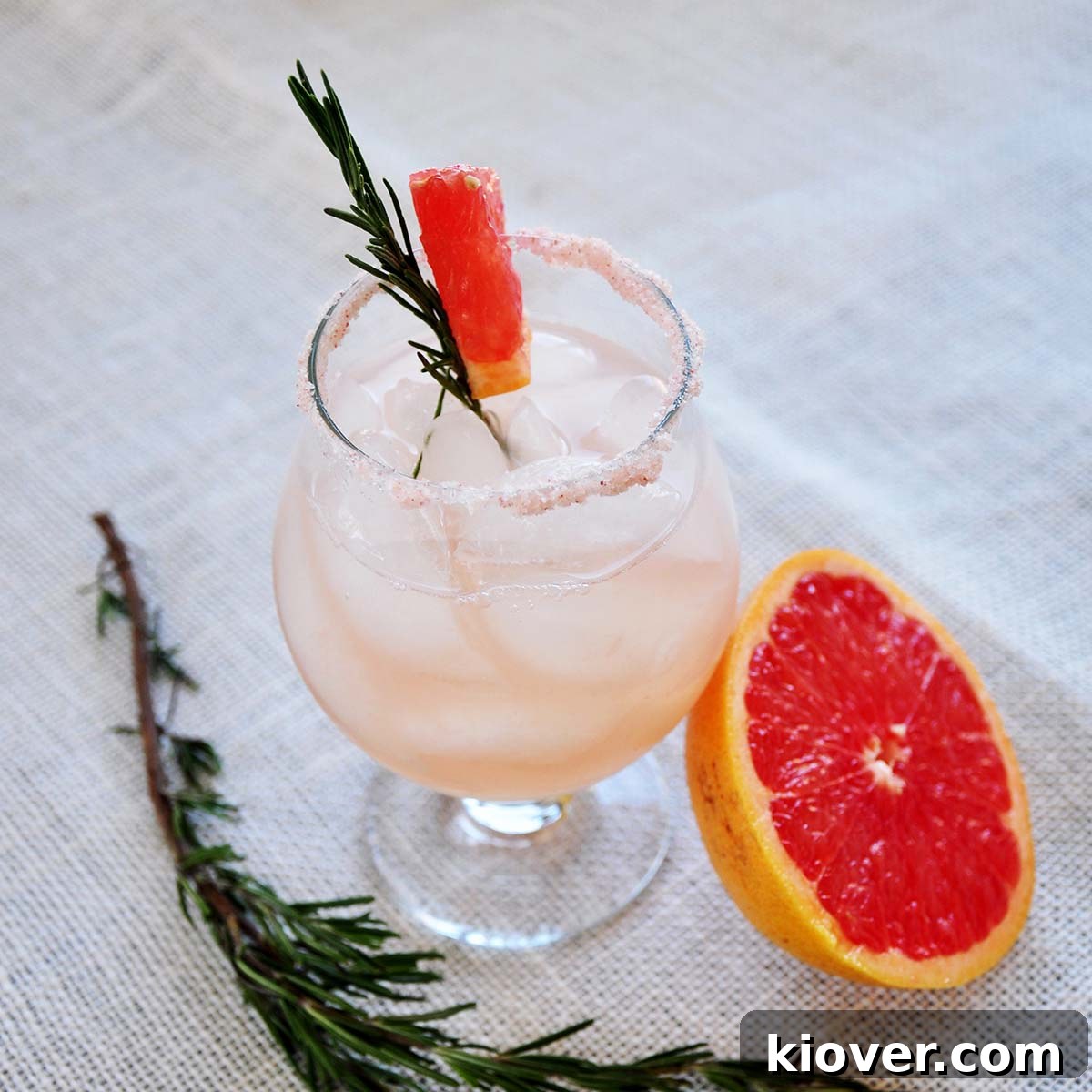 A stunning Rosemary Infused Salty Dog cocktail on a textured mat, garnished with a fresh rosemary sprig and a slice of grapefruit nearby.