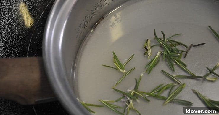 Fresh rosemary sprigs steeping in warm simple syrup in a saucepan, highlighting the infusion process for the cocktail.