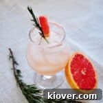 Rosemary Infused Salty Dog on a mat. Half a grapefruit close by and a sprig of rosemary on the side