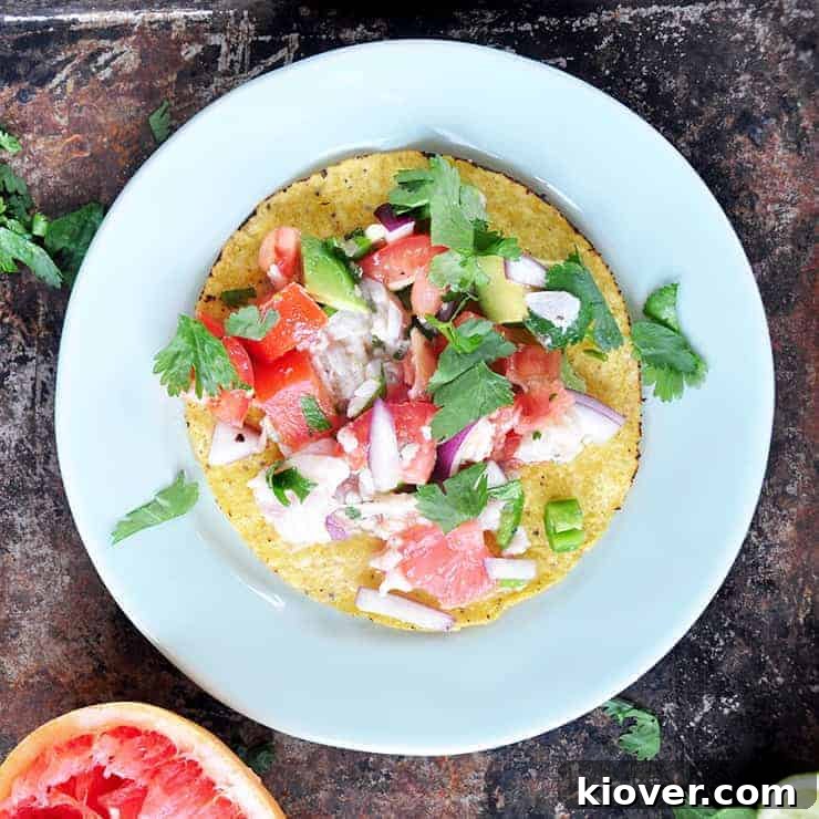 Grapefruit ceviche on a tostada on a white plate with a grapefruit in the background and cilantro sprinkled on the plate