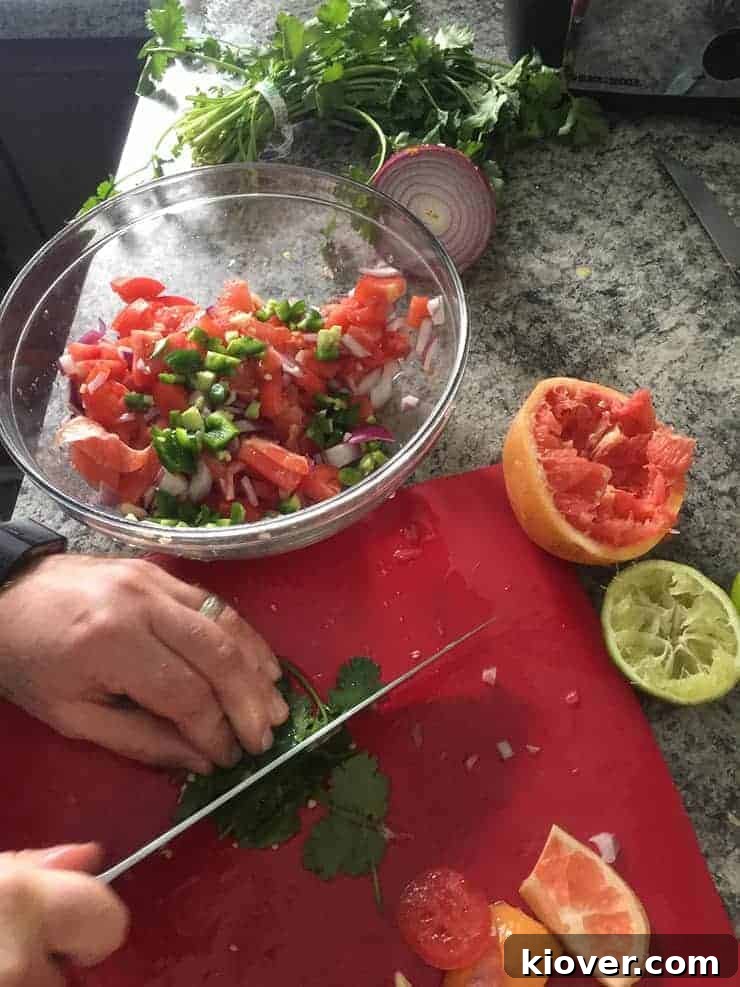 Cutting fresh cilantro on a red cutting board with spent lime and grapefruit in the background, next to a bowl of fresh ingredients
