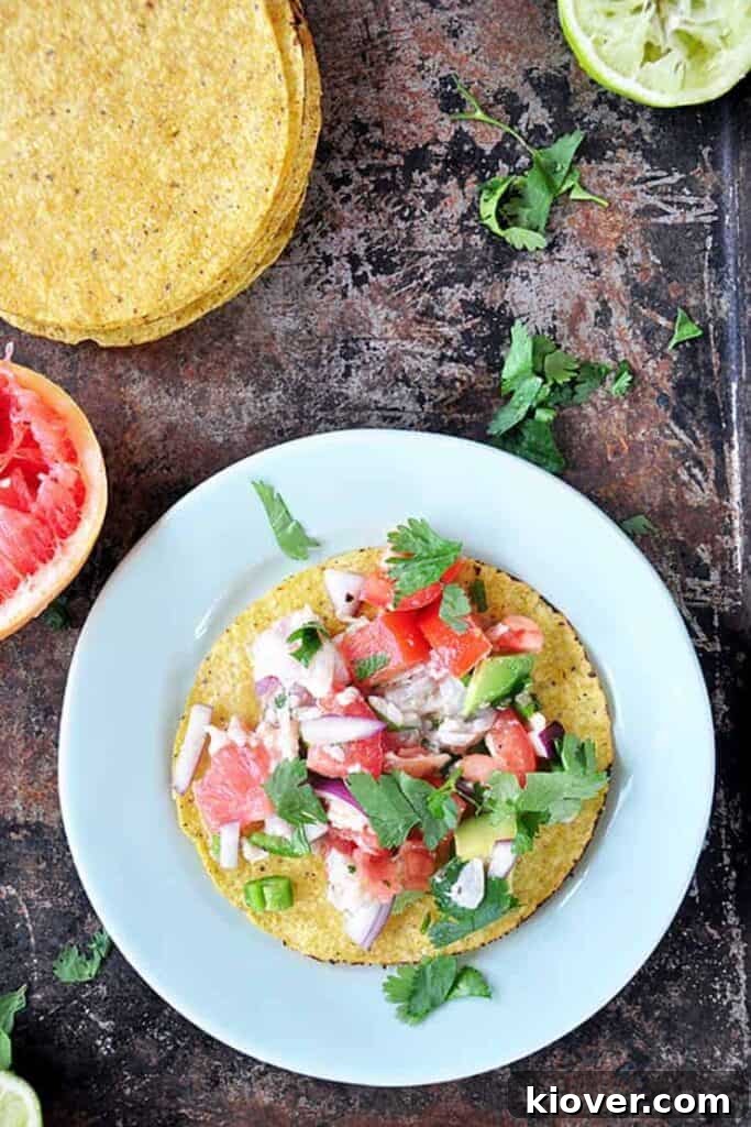 Grapefruit ceviche artfully arranged on a tostada, presented on a light green plate with cilantro, fresh tostadas, a spent lime, and a whole grapefruit in the background