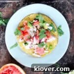 Grapefruit ceviche on a tostada that is also on a white plate with a grapefruit in the background and cilantro sprinkled on the plate
