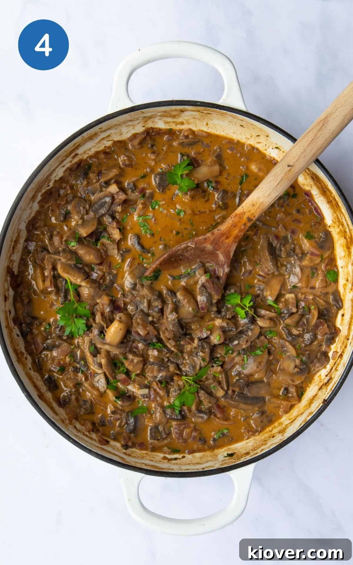Finished One-Pot Vegan Mushroom Stroganoff, rich and creamy, ready to be served directly from the pot with a wooden spoon. The pot is artfully displayed on a white marble background, inviting diners to enjoy.