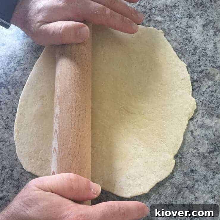 A rolling pin skillfully flattens bread dough on a work surface, a crucial step in preparing it for making delicate, homemade noodles.