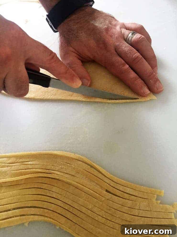 A close-up shot of hands meticulously cutting individual strands of fresh noodle dough with a knife, highlighting the artisanal process.