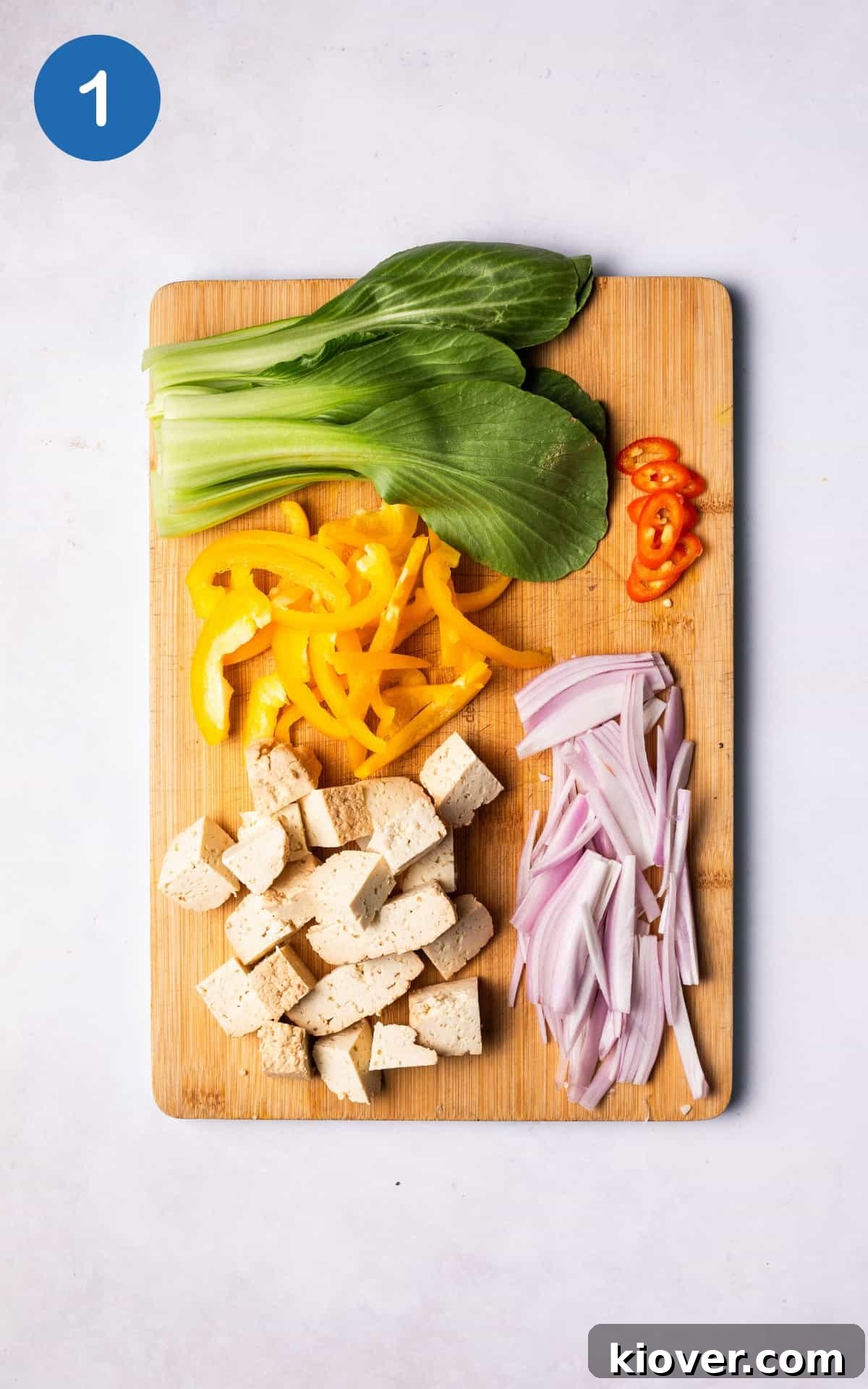 Freshly chopped shallot, bell pepper, pak choi, cubed tofu, and sliced red chili laid out on a cutting board, prepped for cooking.