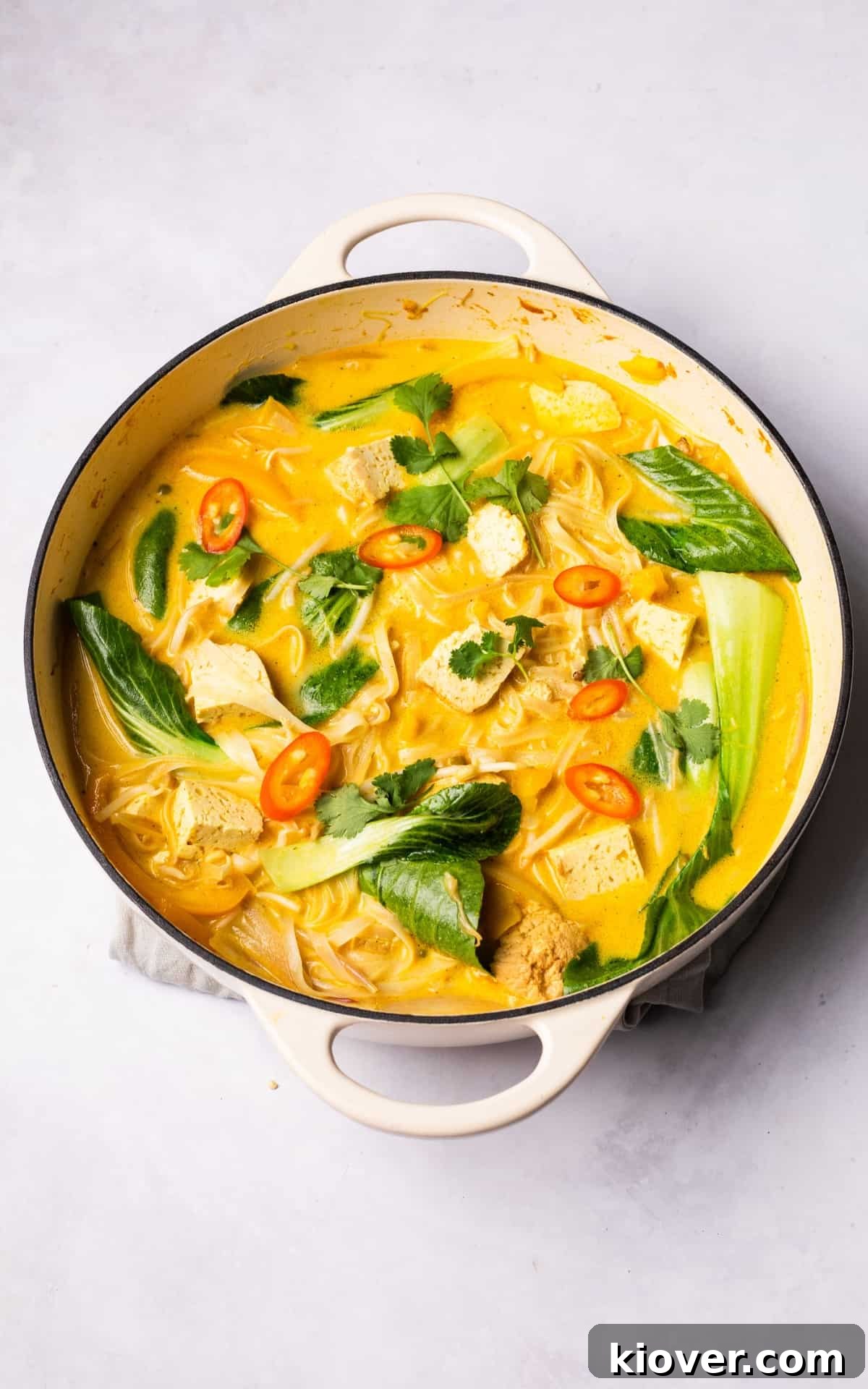 A large pot filled with spicy noodle soup, rich with creamy broth, vegetables, and noodles, ready to be served, highlighting its comforting appeal.