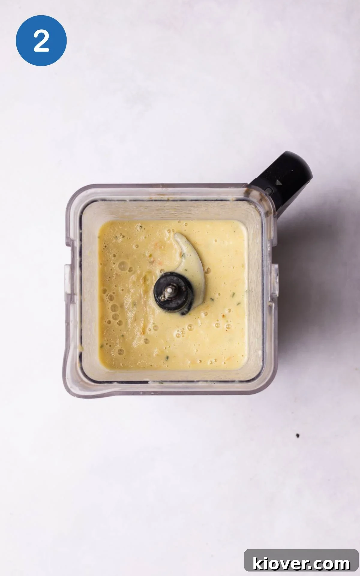 A blender filled with roasted vegetables, vegetable stock, and cream, ready to be blended into a smooth soup.