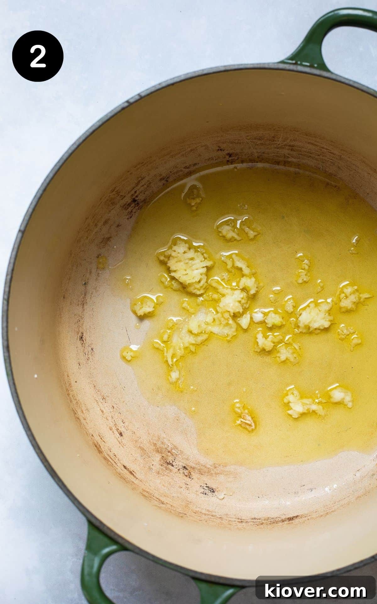 Large cast iron pot with olive oil and crushed garlic gently frying, releasing its aroma.