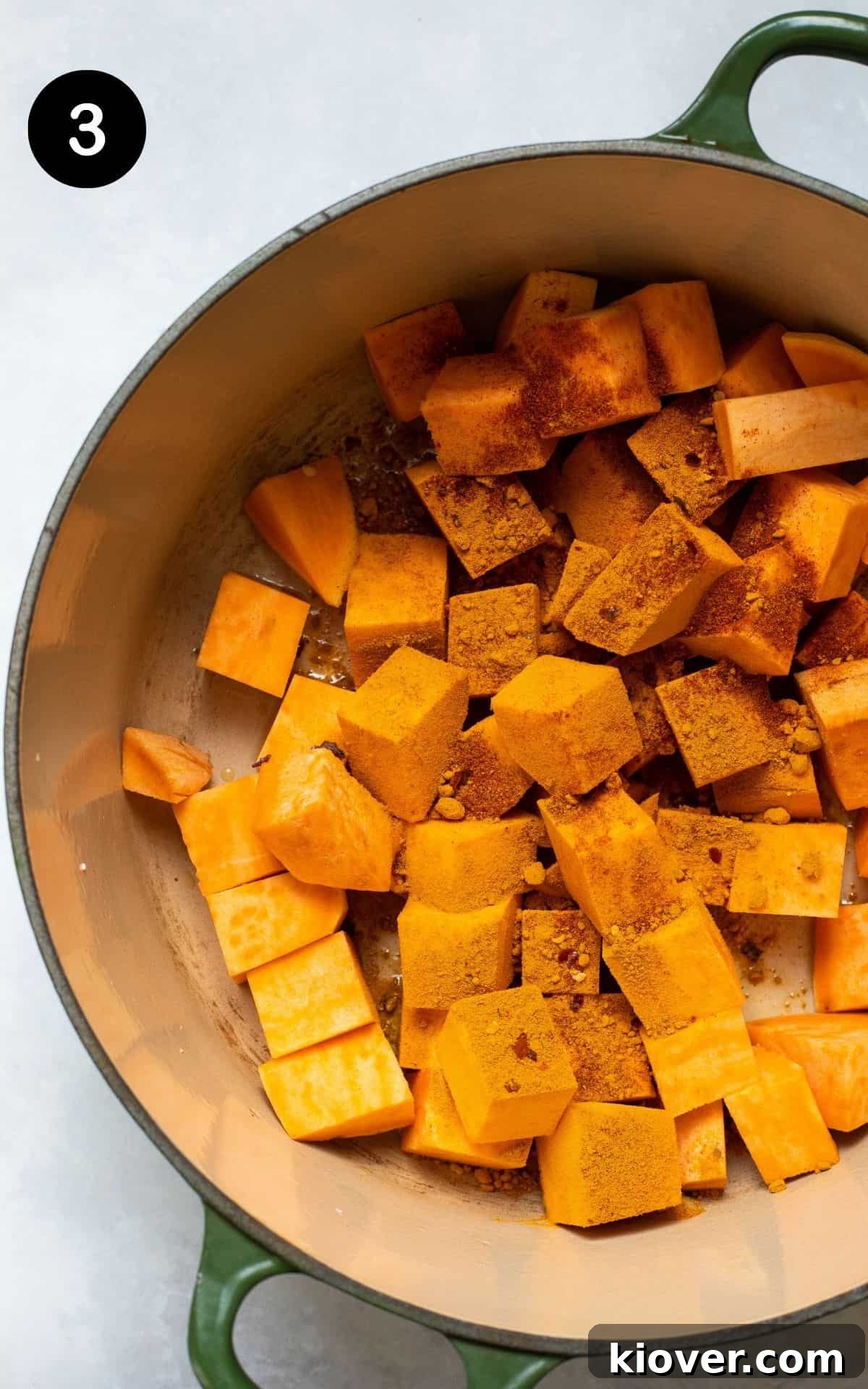 Cast iron pot with chopped sweet potato and various spices frying together, coating the vegetables.