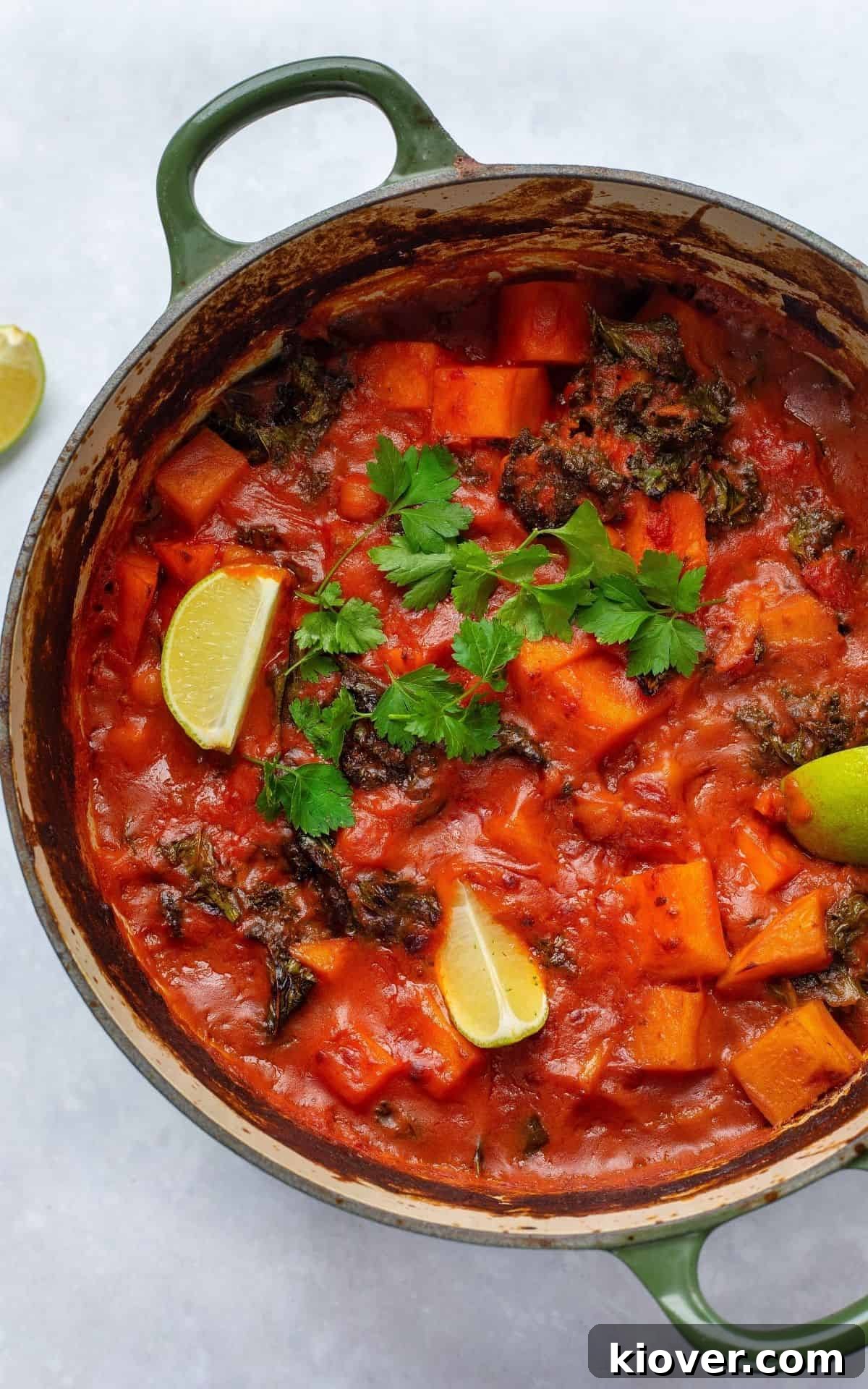 Sweet Potato & Chickpea Curry cooked in a large cast iron pot, garnished with fresh herbs and a swirl of cream.
